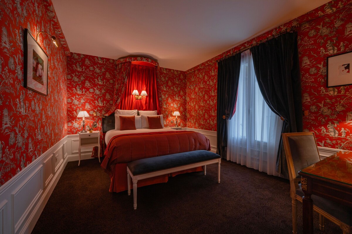 Una habitación de hotel con una cama grande, un banco, un escritorio y una silla.