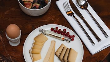 Un desayuno con un plato de queso, un bol de fruta y una taza de café sobre una mesa de madera.