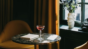 A round table with a glass of red wine, a chair, and a vase with flowers by a window. - Hôtel de Buci (Paris)
