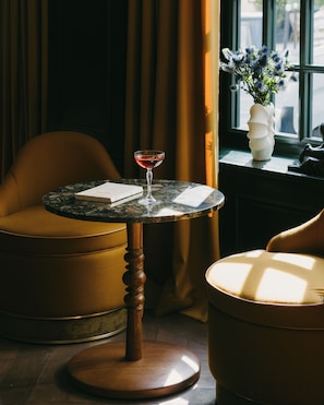 A round table with a glass of red wine, a chair, and a vase with flowers by a window. - Hôtel de Buci (Paris)