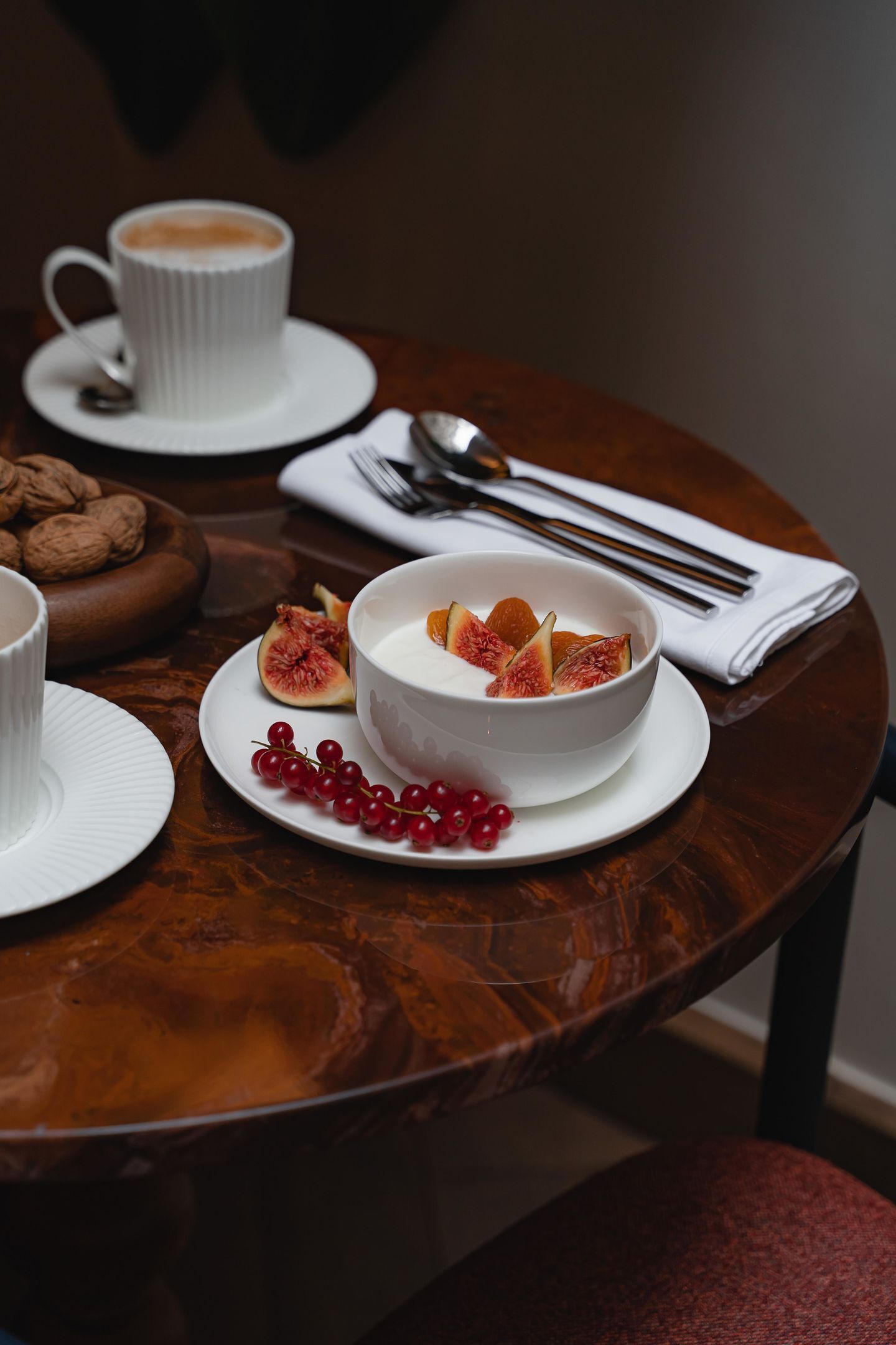 Une table à manger avec un bol de yaourt garni de fruits, une tasse de café et une assiette de biscuits.