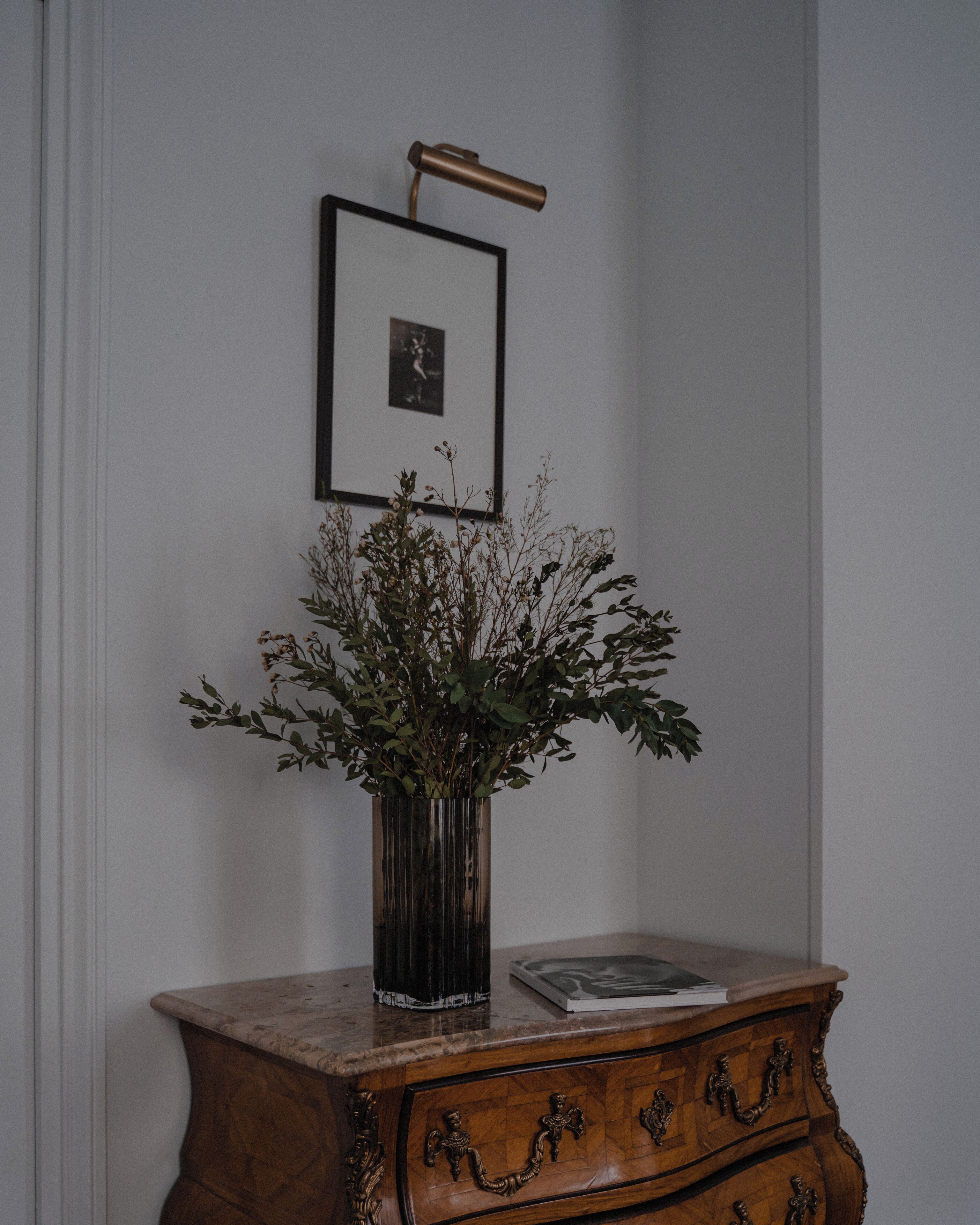 A wooden dresser with a vase of dried plants and a framed picture on top.
