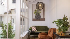 Ein gemütliches Interieur mit einem grünen Sofa, einem braunen Sessel und einem schwarzen Metallregal mit Pflanzen.