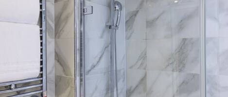 A modern bathroom with a glass-enclosed shower, a towel rack with white towels, and marble tiles.