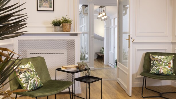 Ein Zimmer mit Kamin, zwei grüne Sessel mit gemusterten Kissen, ein kleiner Tisch und ein gerahmtes Monet-Gemälde an der Wand.