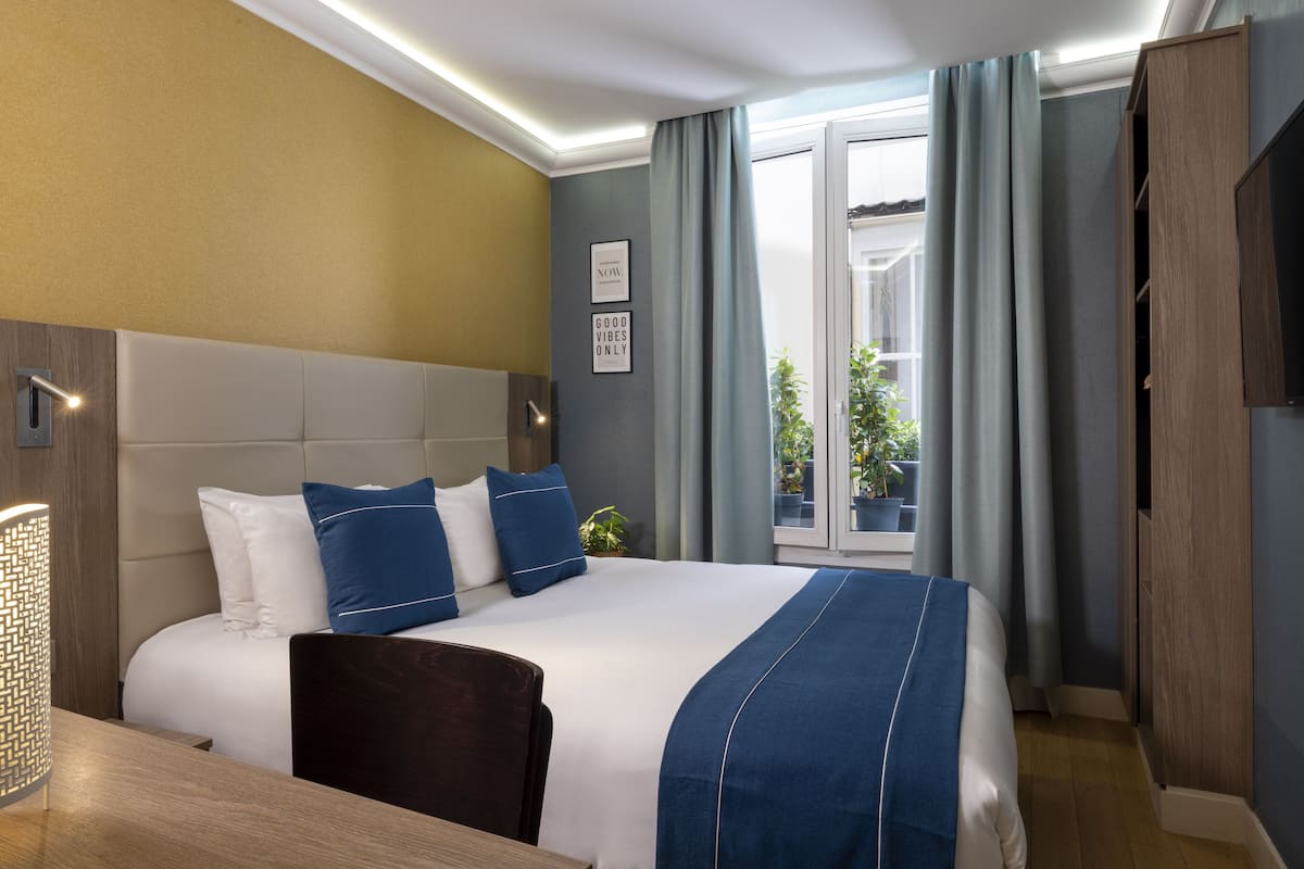 A modern hotel room with a large bed, a bedside table, a desk, and a view of the outdoors.