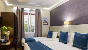Ein Hotelzimmer mit zwei Betten, einem Schreibtisch, einem Stuhl, einer Zimmerpflanze und einem Fenster mit Vorhängen.