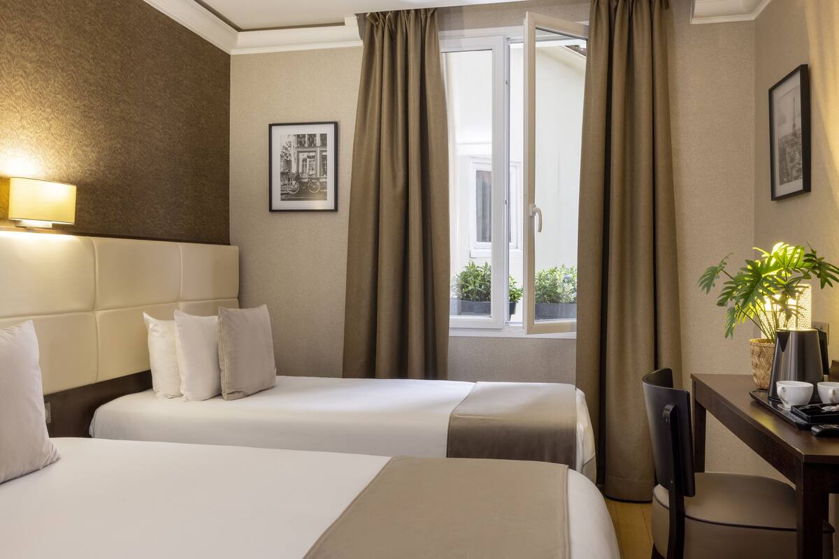 A hotel room with two beds, a desk, a chair, a lamp, and a window with curtains.