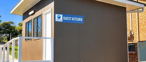 Een gastenkeuken met een bordje, een houten terras en een bakstenen gebouw op de achtergrond.