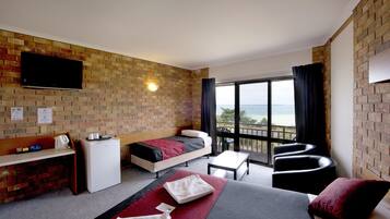 A hotel room with a bed, a desk, a refrigerator, a television, and a balcony with a view.