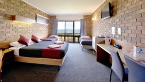Habitación de hotel con dos camas, un escritorio, un televisor y un balcón con vista al mar.