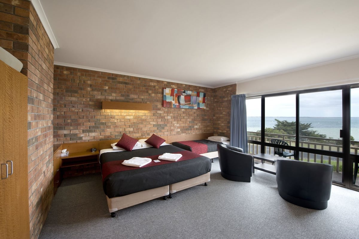 A hotel room with a brick wall, a bed with pillows, a desk, and a balcony with a view.