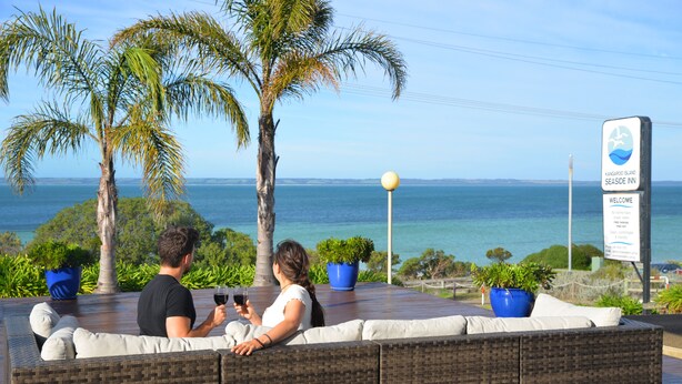 Una pareja descansando en un sofá de mimbre con vista al mar, con un cartel del Kangaroo Island Seaside Inn al fondo.