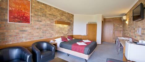 Ein Hotelzimmer mit Backsteinwand, einem Bett mit roter Bettwäsche, einem Schreibtisch, einem Sessel und einem Fernseher.