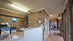 Zona de recepción con pared de ladrillo, mostrador con folletos y vista a un comedor.