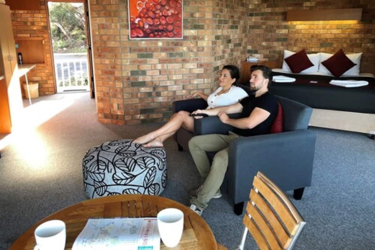 A modern living room with a brick wall, a sofa, a wooden ottoman, and a table with two cups.