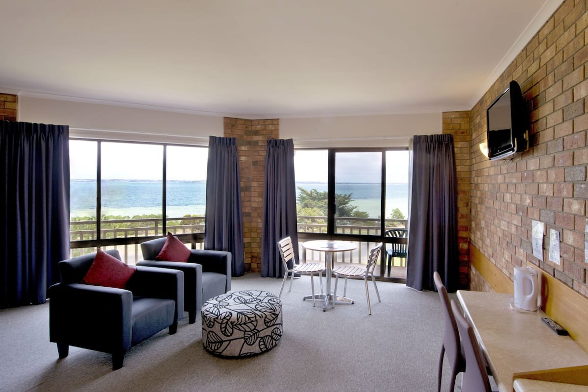 A hotel room with a balcony, a TV mounted on the wall, and a view of the ocean.