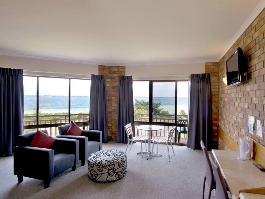 A hotel room with a balcony, a TV mounted on the wall, and a view of the ocean.