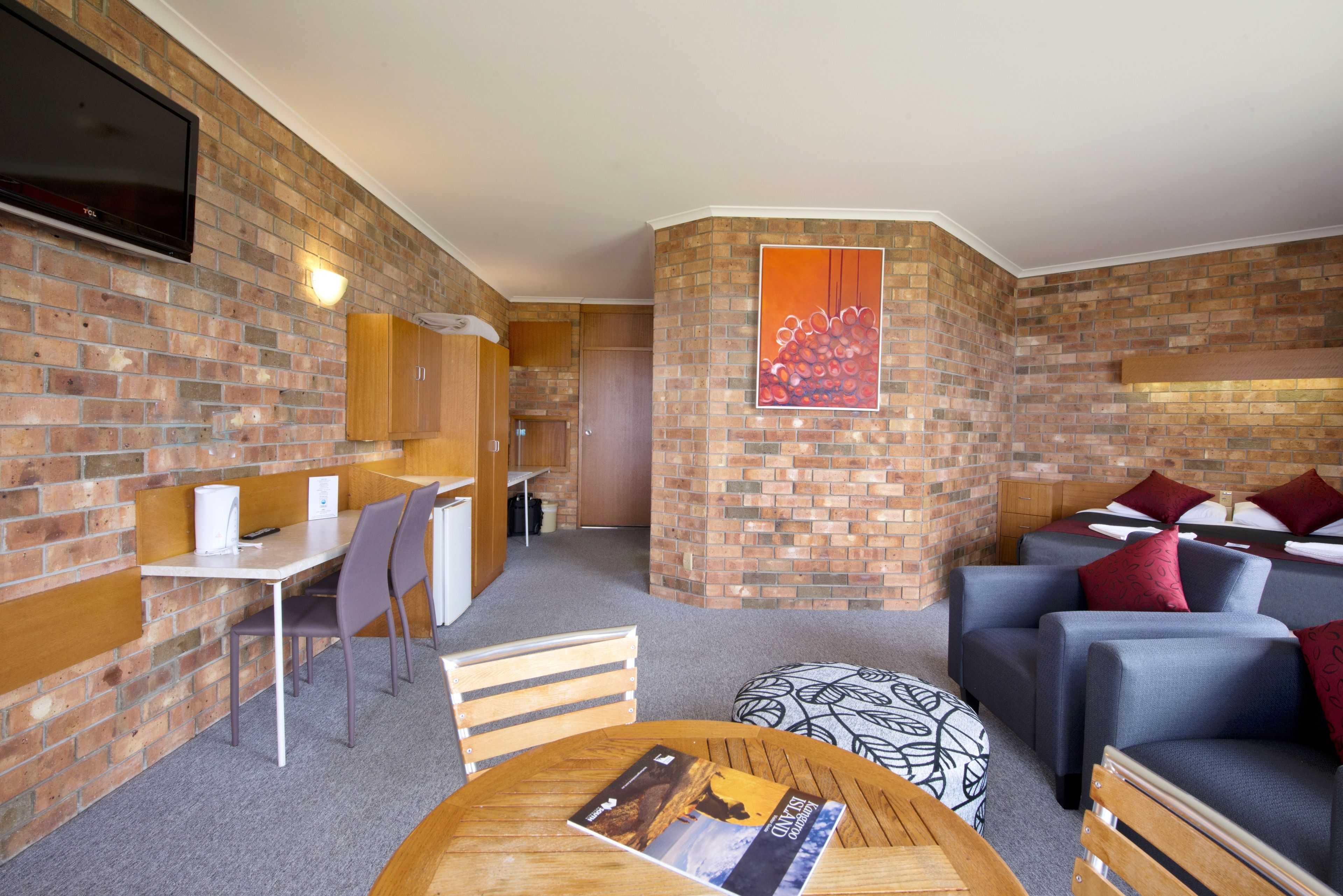 A modern room with a brick wall, a flat-screen TV, a dining area, and a seating area with sofas and cushions.