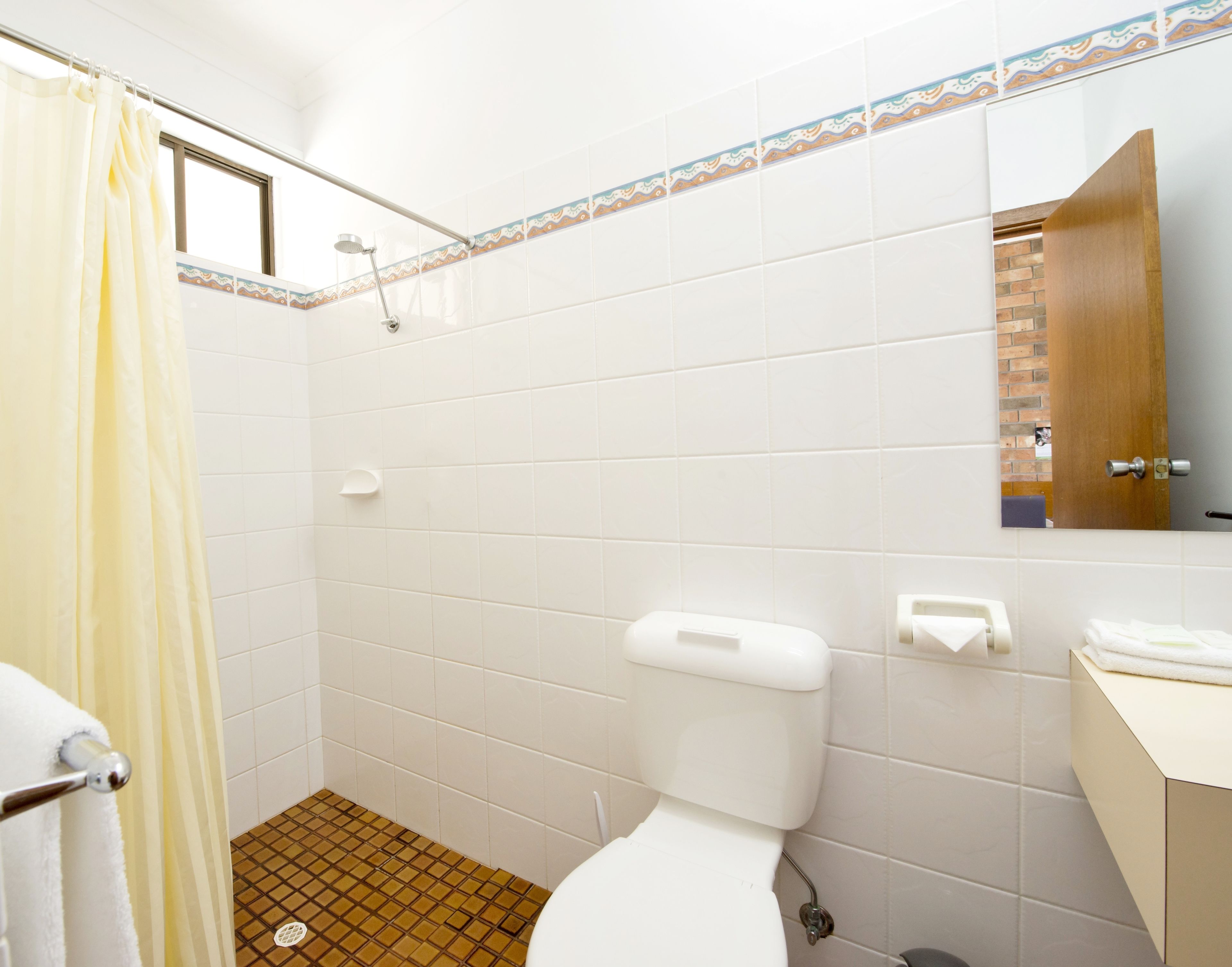A bathroom with white tiles, a shower curtain, a toilet, a sink, and a mirror.