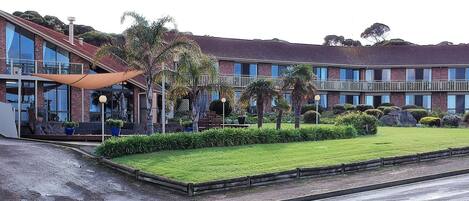 Un edificio moderno con fachada de vidrio, entrada cubierta y césped bien cuidado.