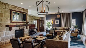 A spacious living room with a stone fireplace, comfortable seating, and a large window providing natural light. - Spicers Guesthouse (Pokolbin)