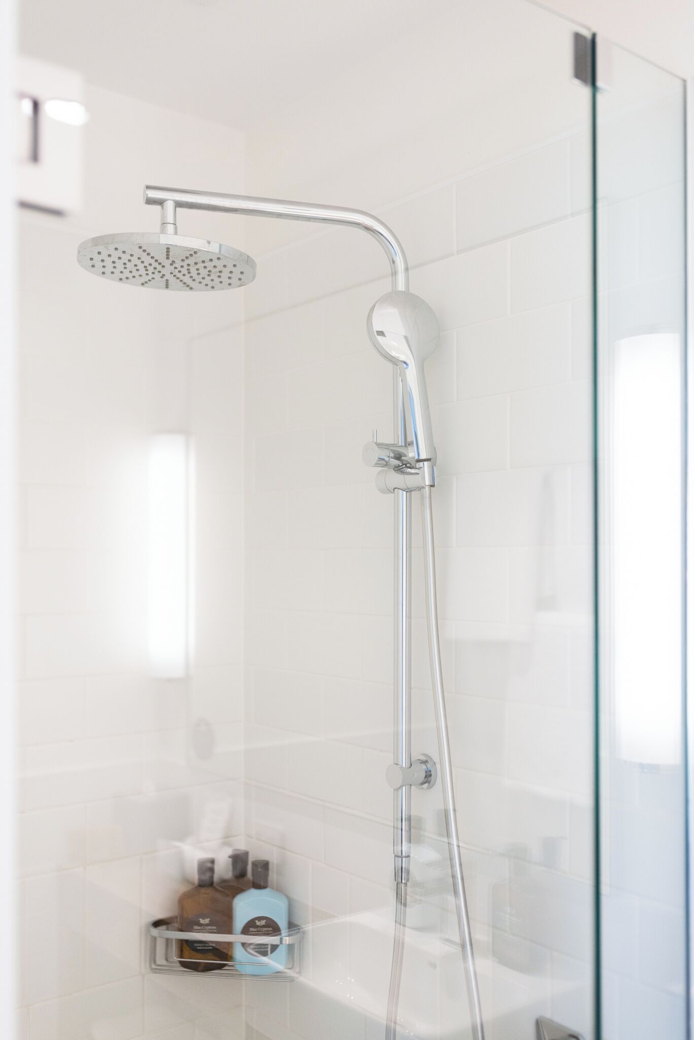 A modern shower with a handheld showerhead and a wall-mounted faucet, a glass shower enclosure, and a small shelf with toiletries.