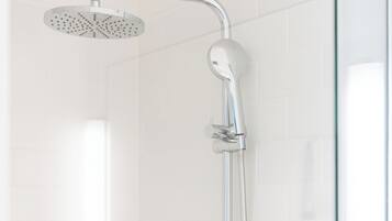 A modern shower with a handheld showerhead and a wall-mounted faucet, a glass shower enclosure, and a small shelf with toiletries.