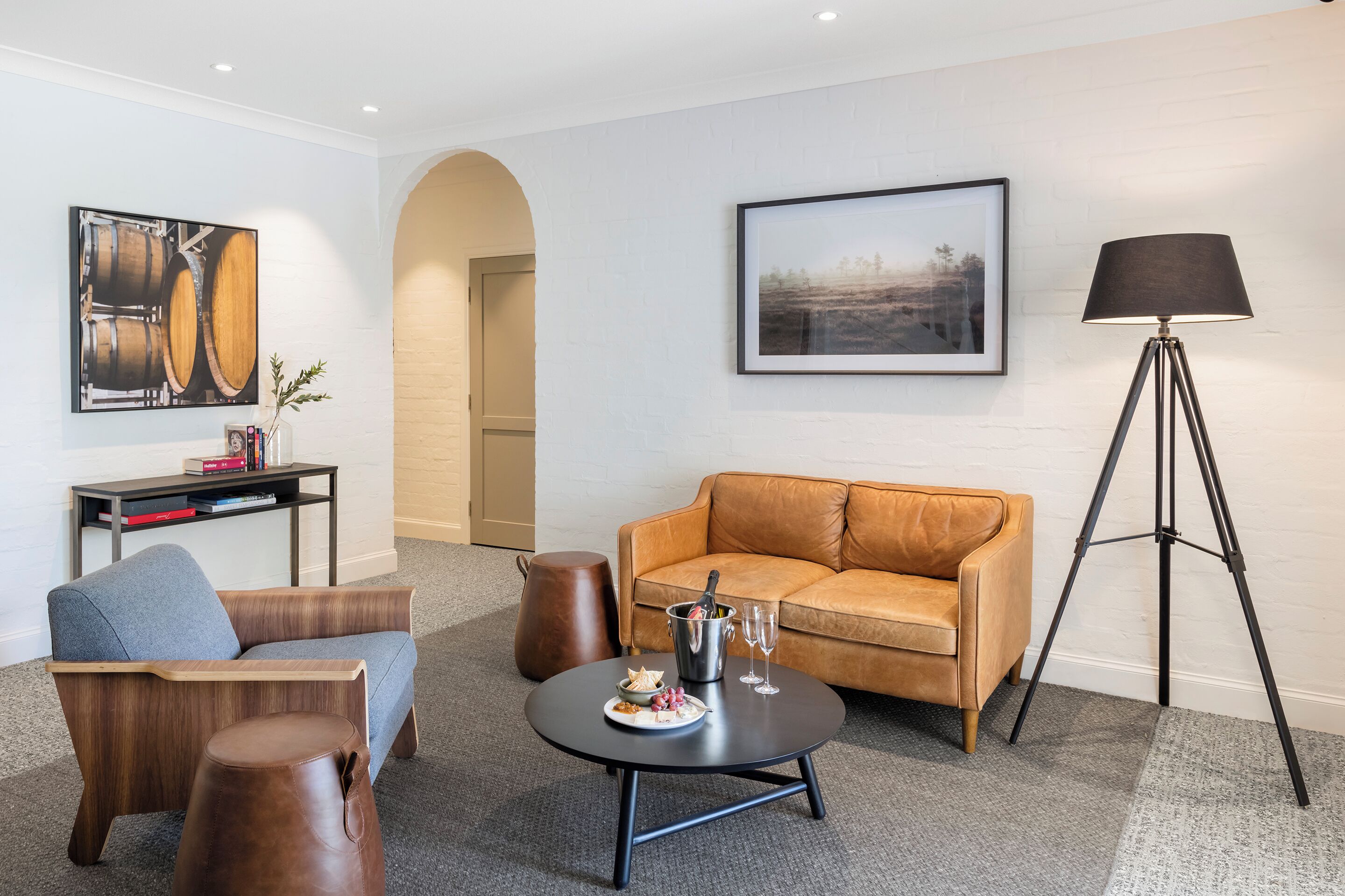 A modern living room with a leather sofa, a grey armchair, a coffee table with a bottle and glasses, and a floor lamp.