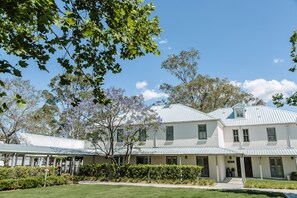A two-story white building with a green roof, surrounded by well-maintained lawns and trees. - Spicers Guesthouse (Pokolbin)
