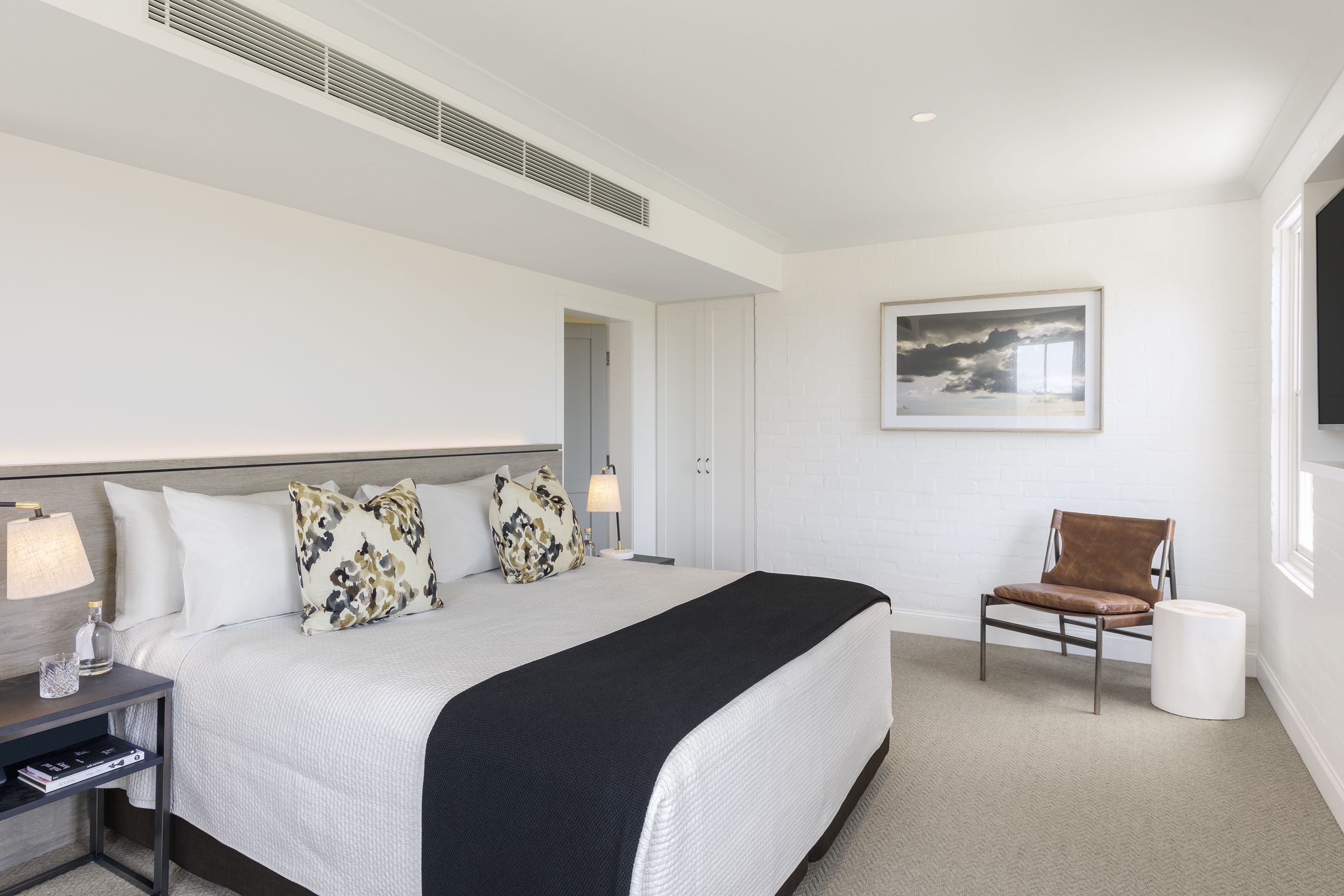 A hotel room with a large bed, a chair, a nightstand, a lamp, and a framed picture on the wall.
