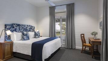 A bedroom with a bed, a desk, a chair, a nightstand, and a ceiling fan.