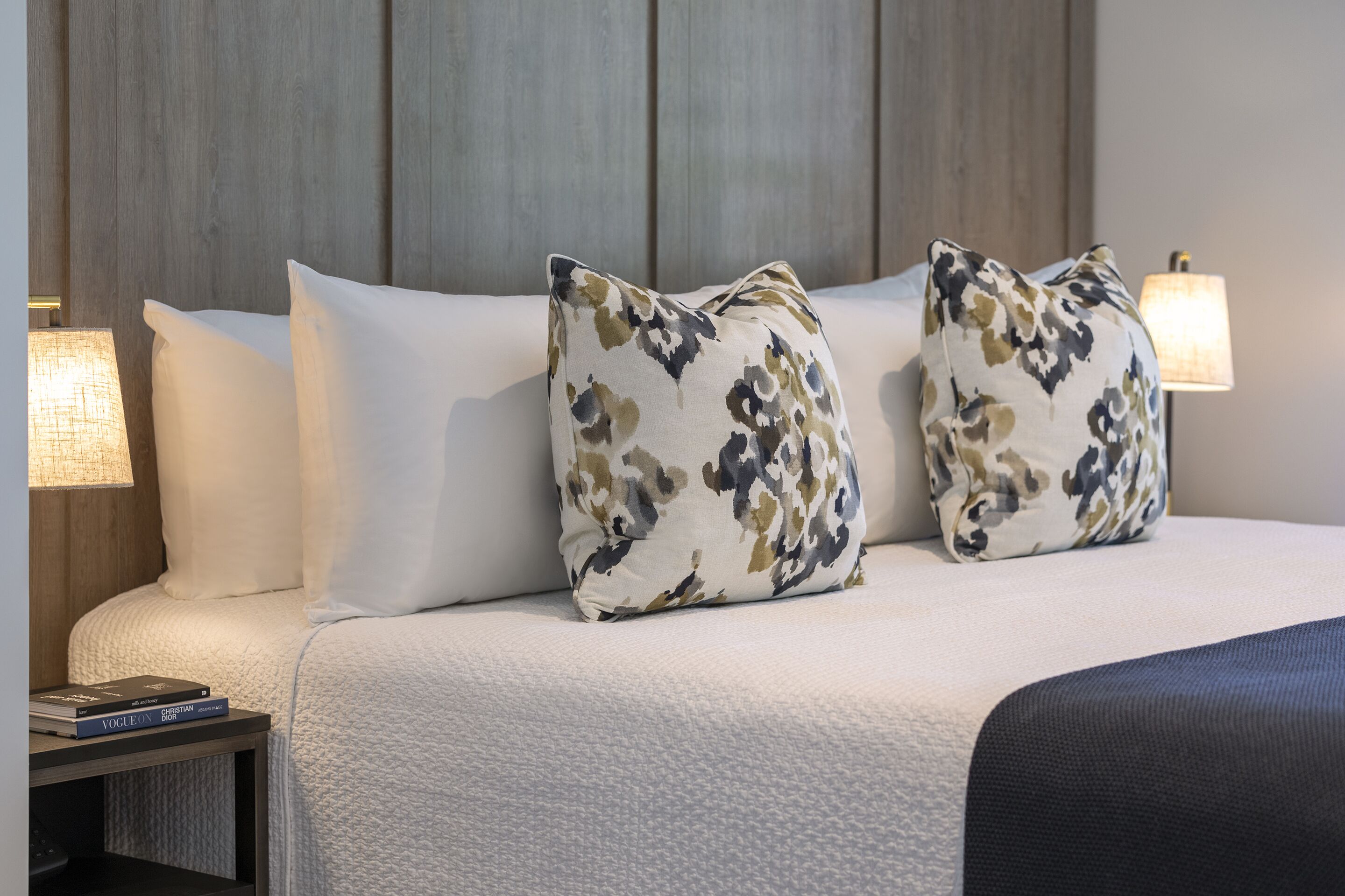 A neatly made bed with two decorative pillows, a bedside lamp, and a book on a nightstand.