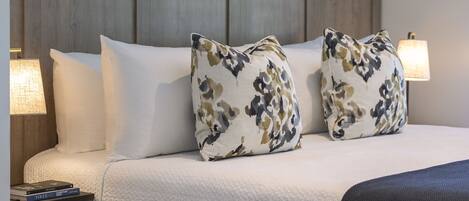 A neatly made bed with two decorative pillows, a bedside lamp, and a book on a nightstand.