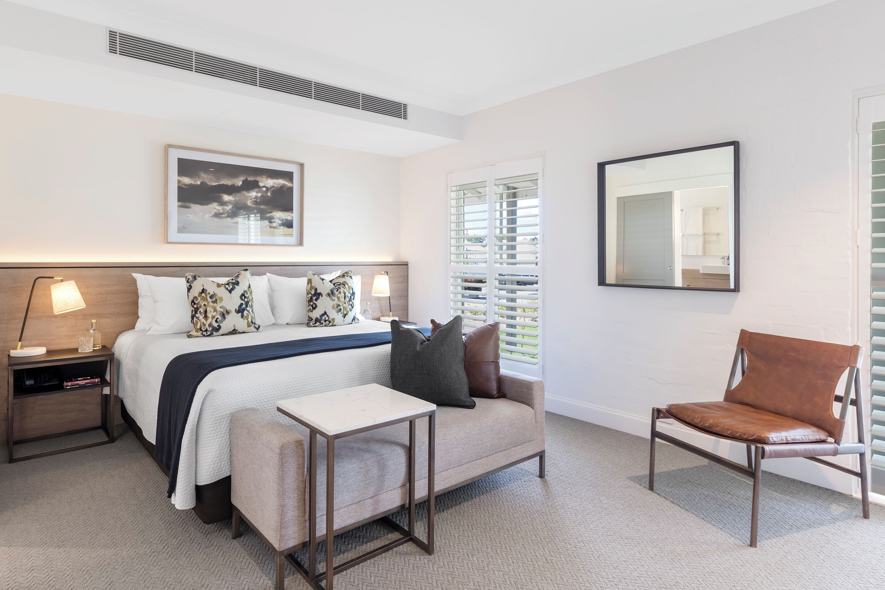A modern bedroom with a bed, bedside tables, a desk, a chair, and a large window with blinds.