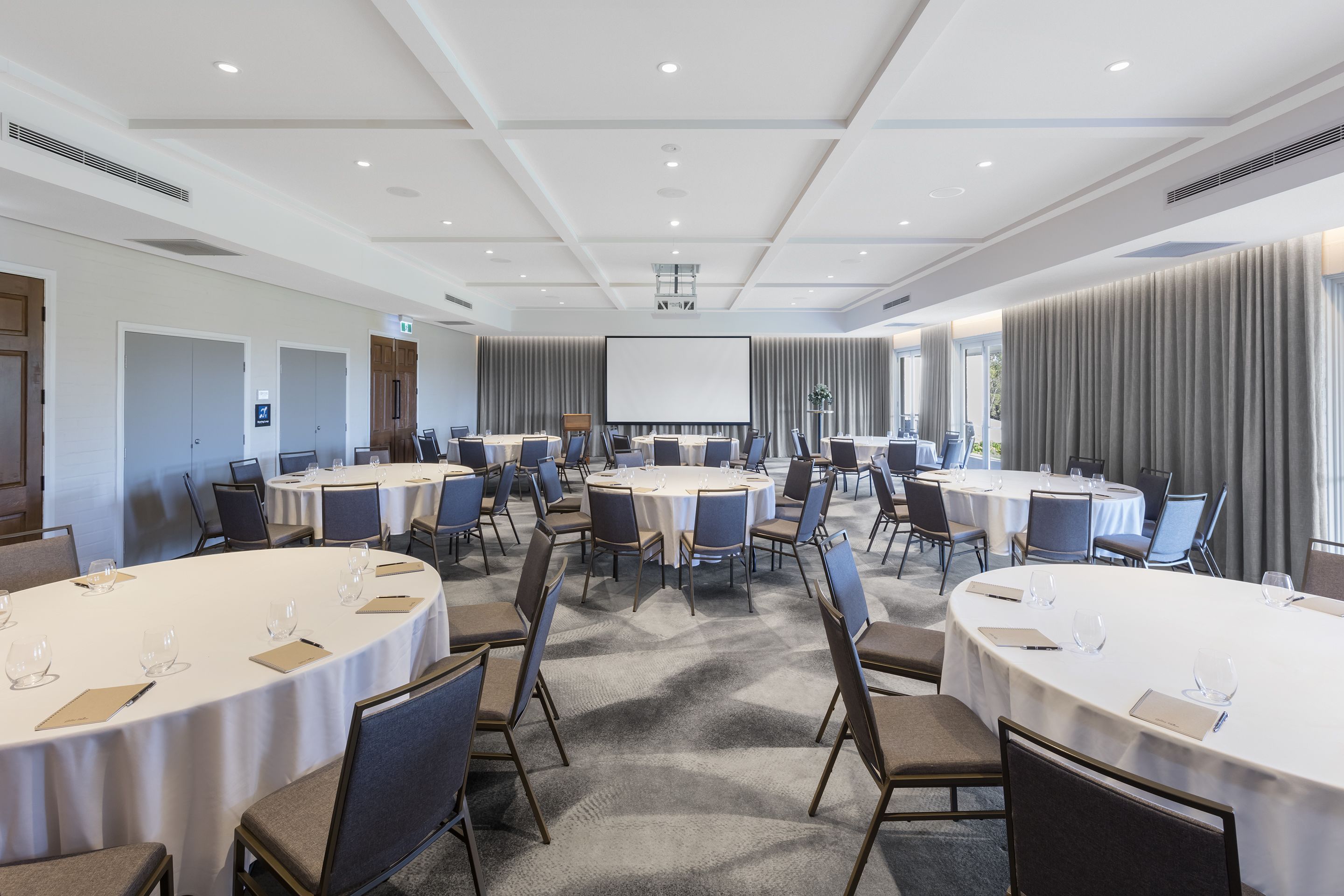 A conference room with multiple round tables, chairs, and a large screen.