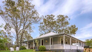 A two-story house with a covered porch, a small front yard, and a view of the surrounding trees. - Spicers Guesthouse (Pokolbin)