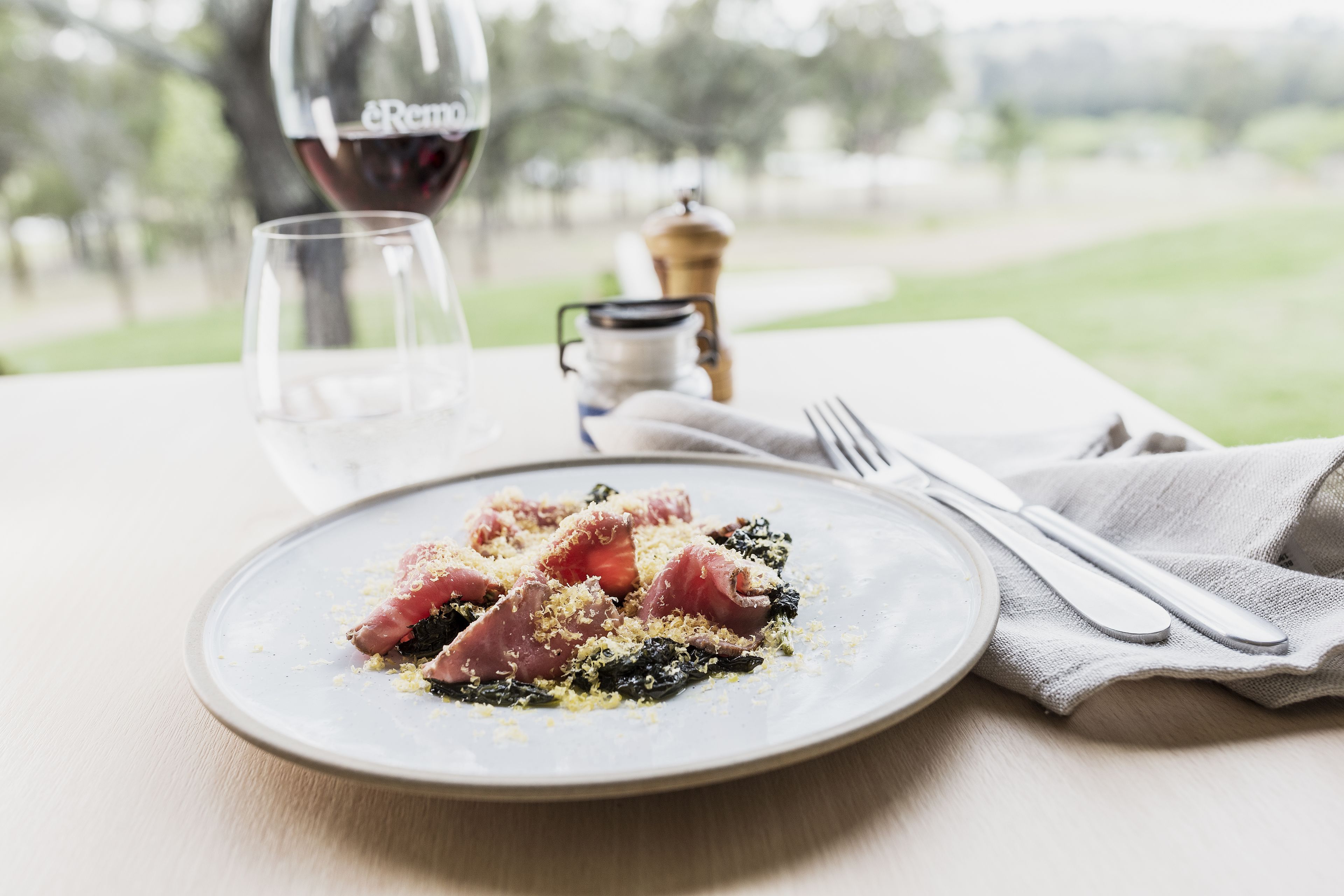 A plate of food on a table with a wine bottle and glasses in the background.