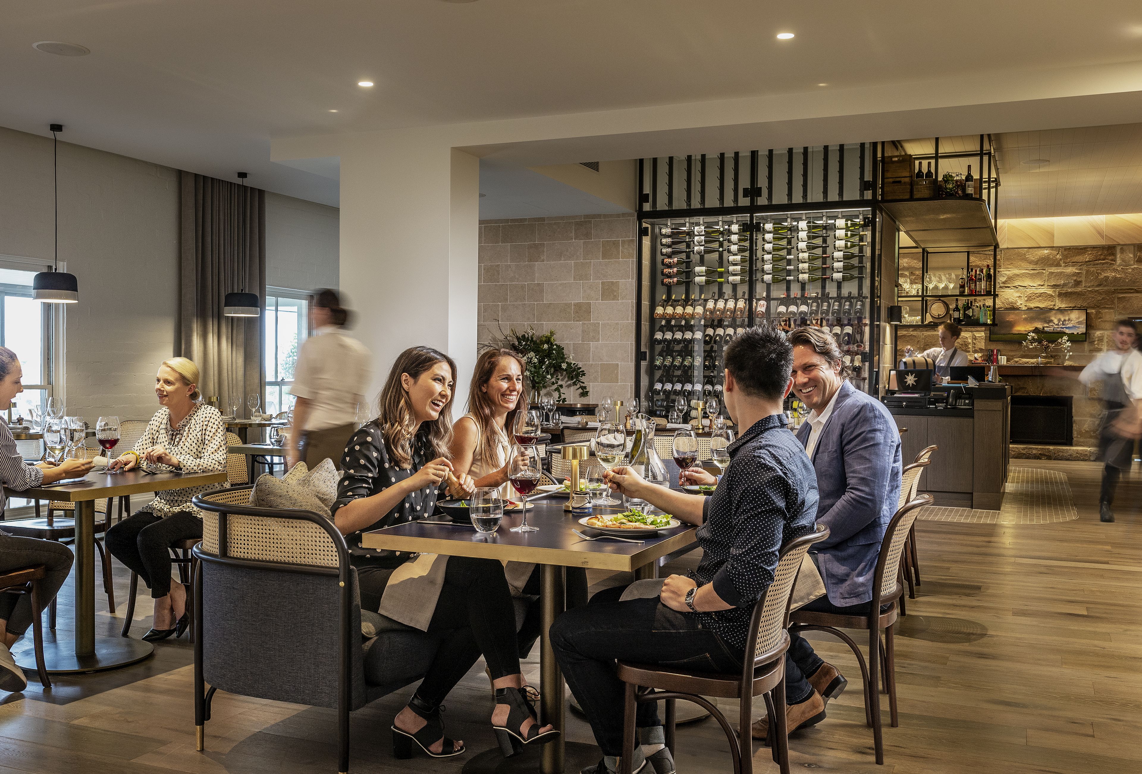 A modern dining area with round tables, comfortable seating, and a wine rack in the background.