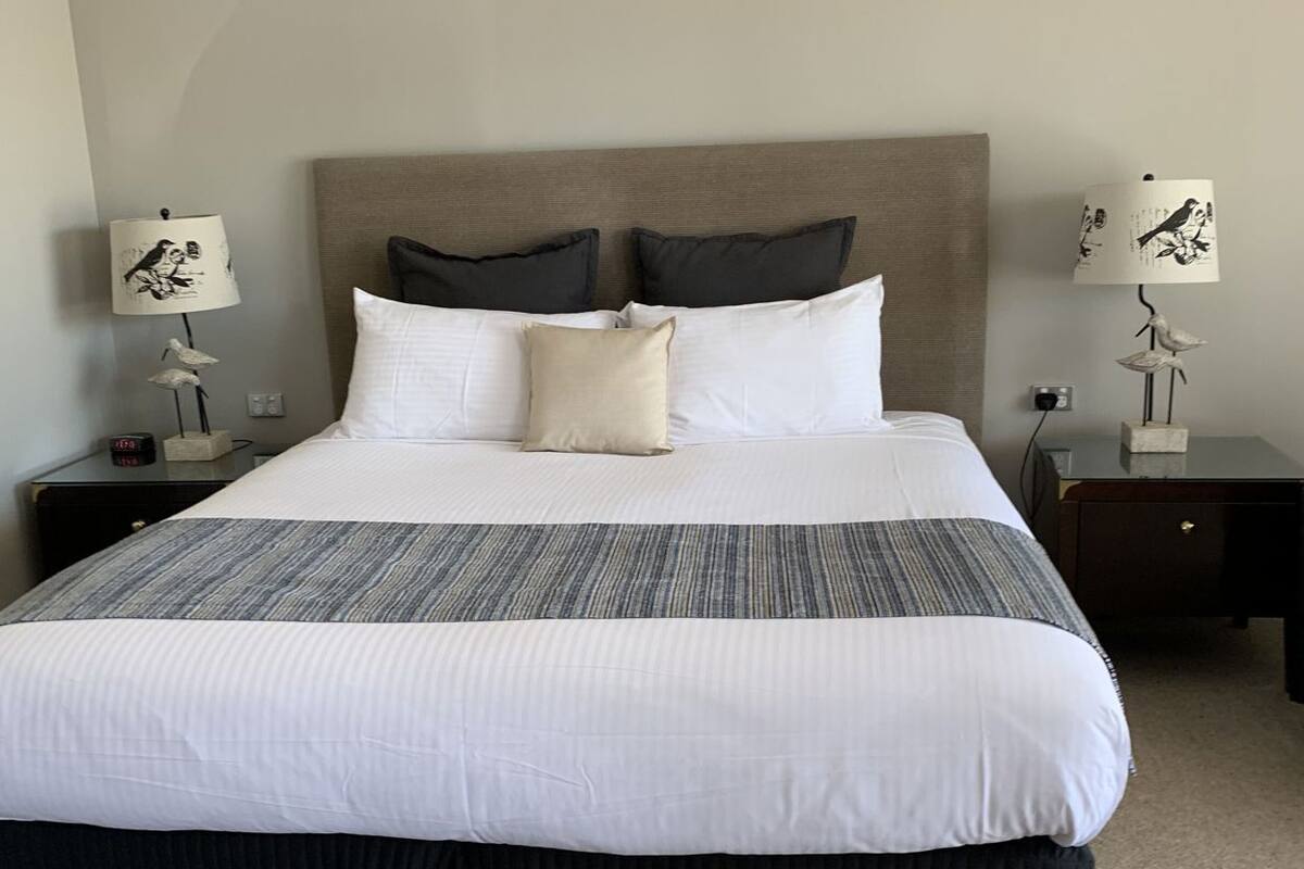 A neatly made bed with a striped bedspread, two pillows, and a nightstand with a lamp and a small decorative item.