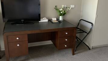 A wooden desk with a flat-screen TV, a vase with flowers, and a chair.