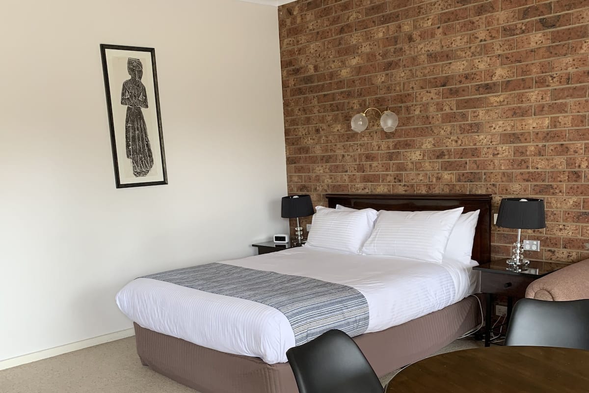 A hotel room with a bed, two bedside tables with lamps, a framed picture on the wall, and a dining table with chairs.