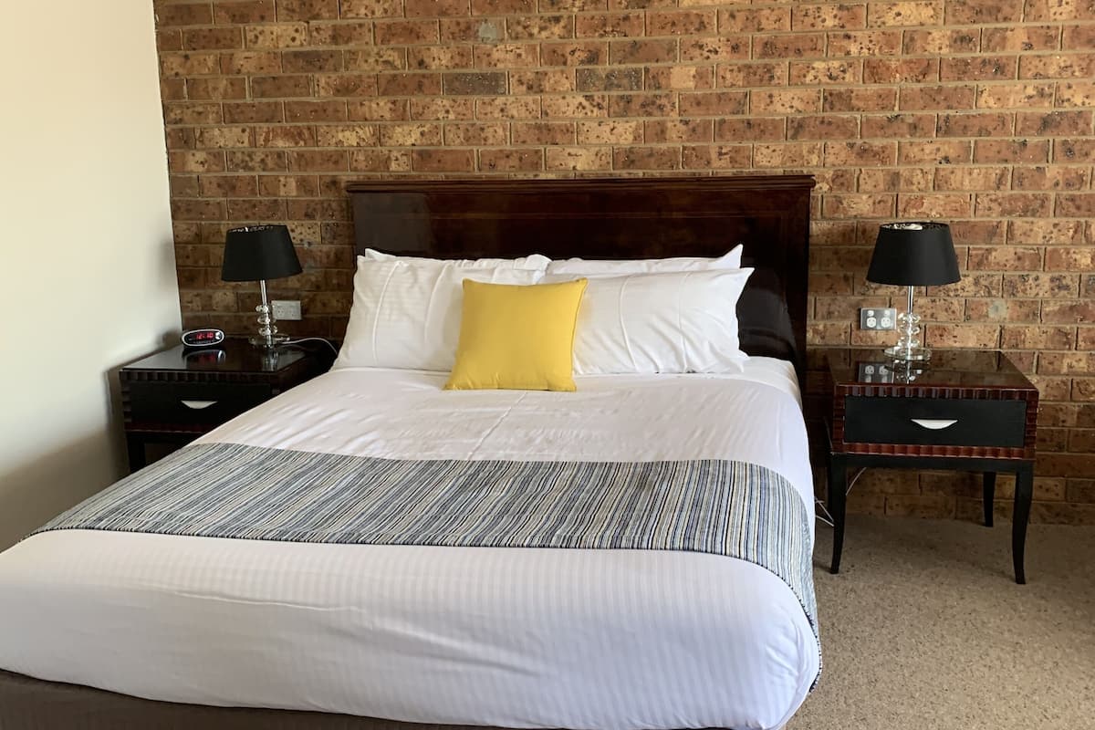A hotel room with a brick-patterned wall, a large bed with white and striped bedding, and two bedside tables with lamps.