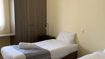 A hotel room with two beds, a wardrobe, a ceiling fan, and a bedside table with a lamp.