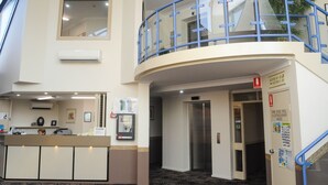 A hotel reception area with a counter, a mirror, an air conditioning unit, a fire hose reel, and an elevator. - Dubbo RSL Club Motel (Dubbo)