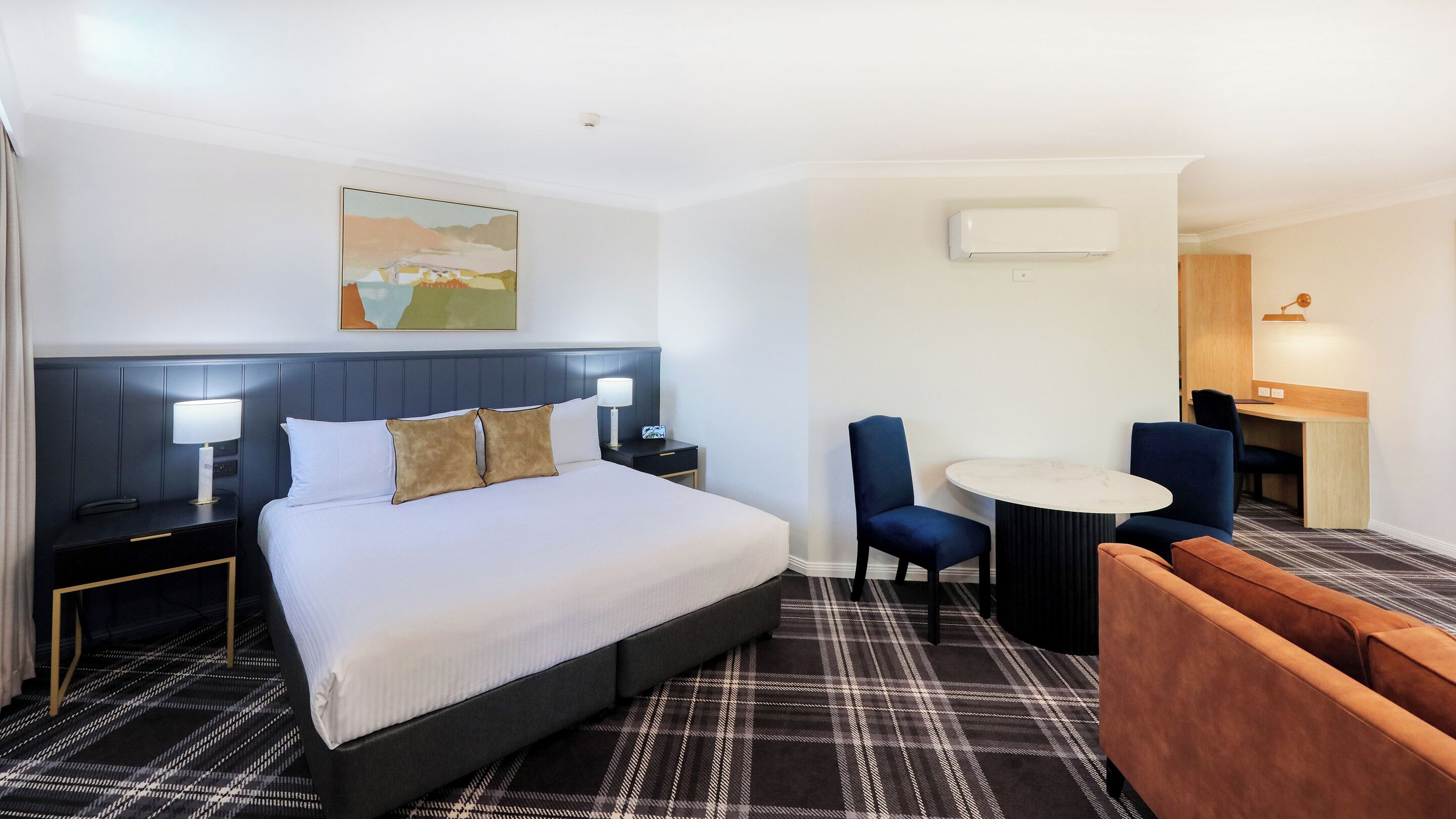 Une chambre d’hôtel comprenant un lit, des tables de chevet, un bureau, deux chaises, une petite table ronde et un tableau au mur.