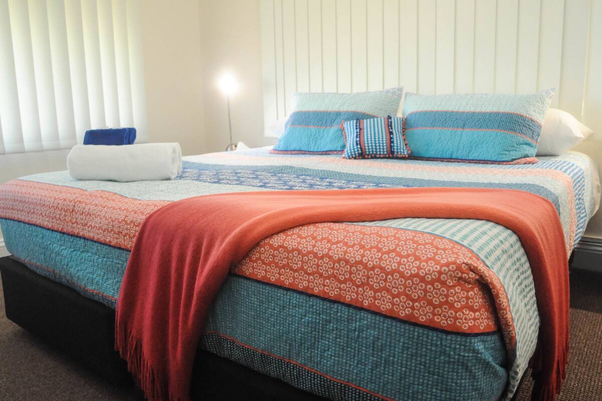 Un lit bien fait, avec une couvre-lit à motifs et des oreillers, une serviette enroulée et une lampe de chevet.
