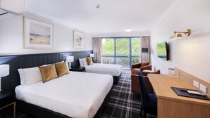 A hotel room with two beds, a desk, a chair, a TV, and a window with a view of greenery. - Dubbo RSL Club Motel (Dubbo)