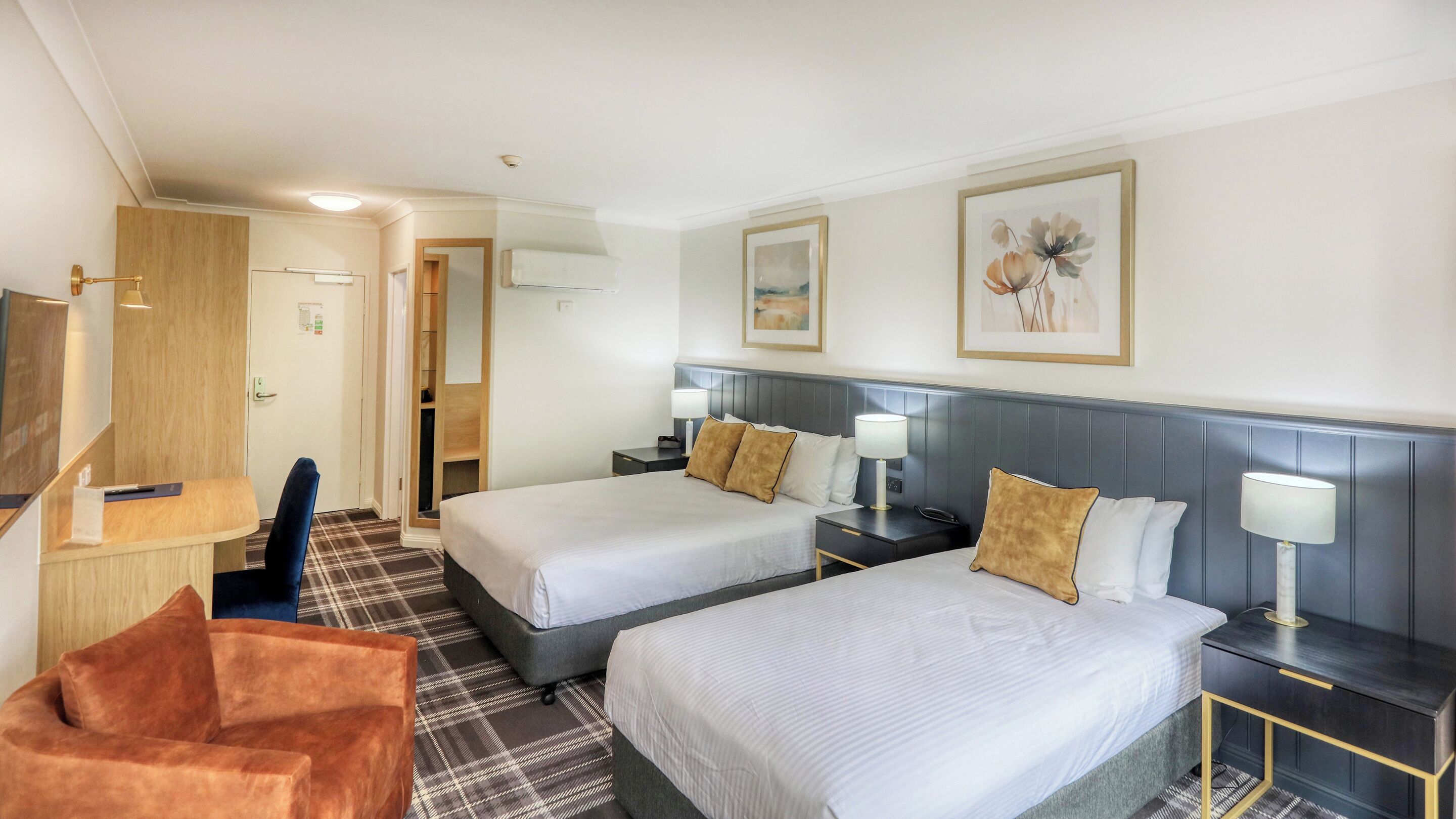 A hotel room with two beds, a desk, a chair, and a large window.
