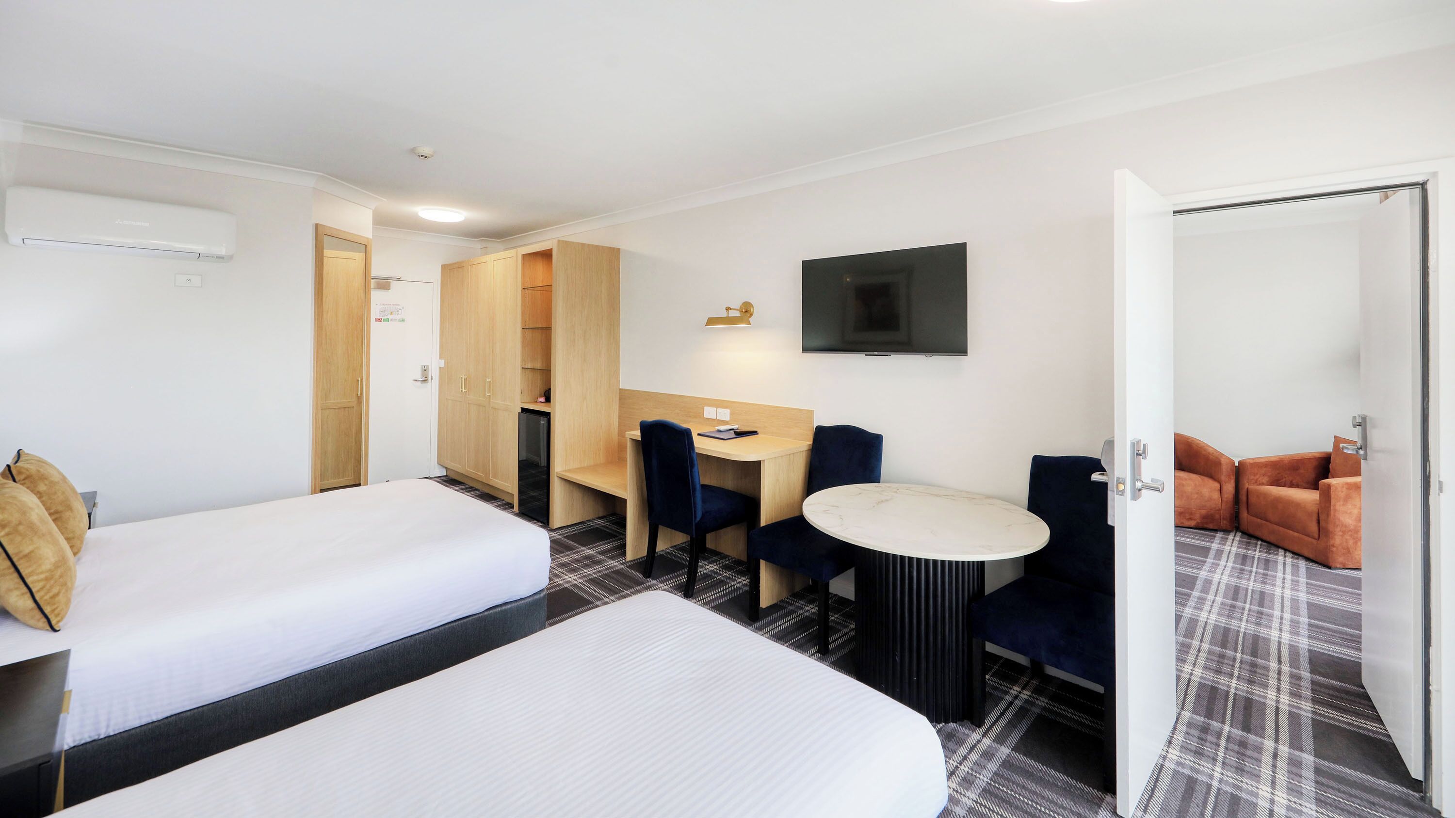 A hotel room with two beds, a desk with a chair, a TV, and a sofa.